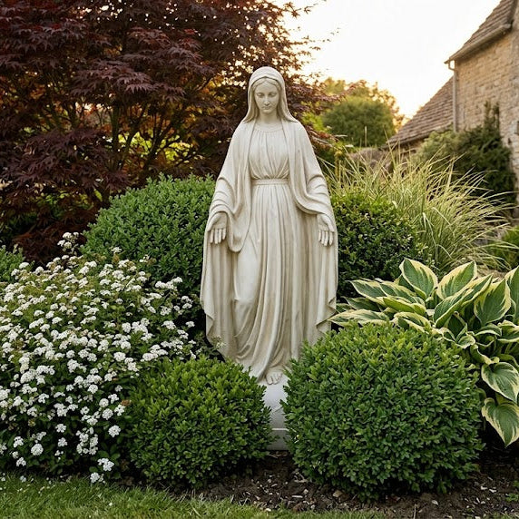 Statue of a Mary-36 H Religious Sculpture  figure in a garden setting with flowers and a building in the background