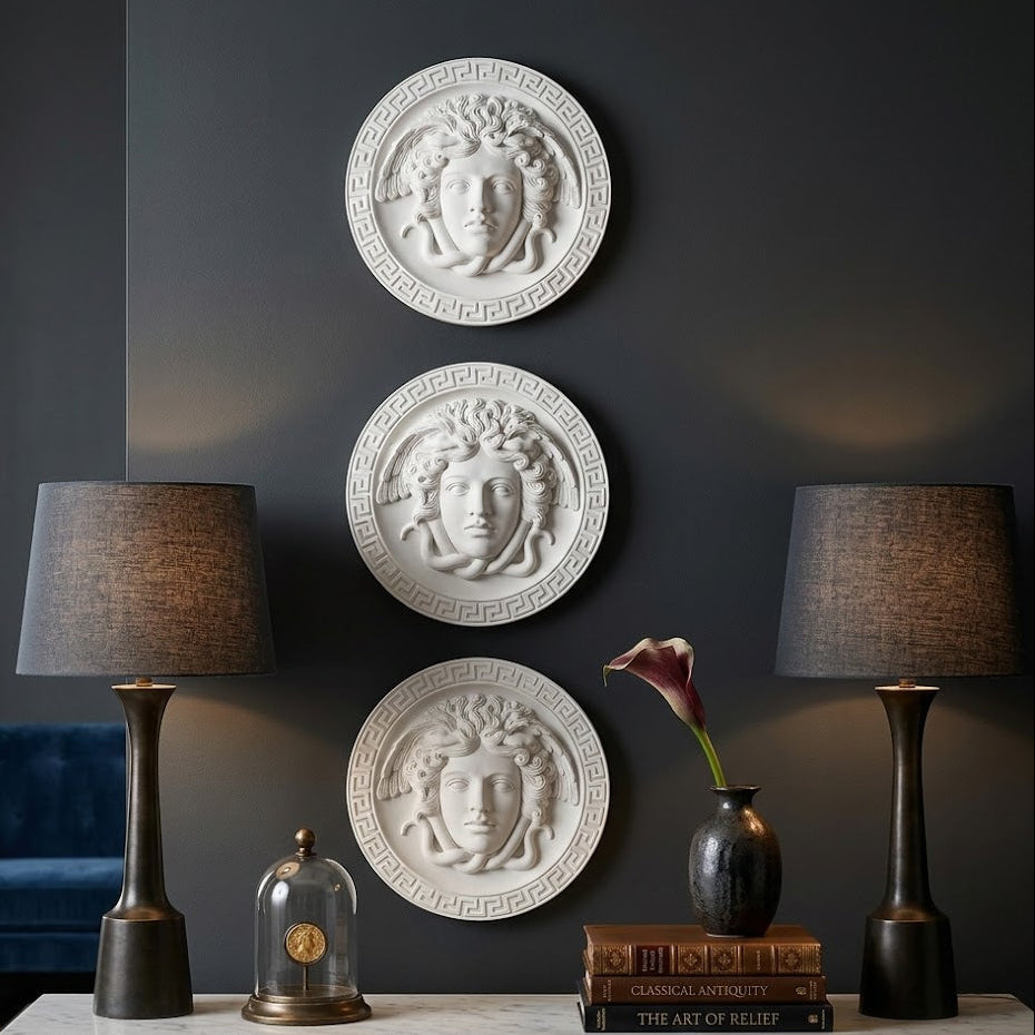 Decorative wall art with face designs on a dark wall, flanked by two lamps and books on a table.