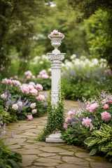 Decorative garden column with flowers on a stone path in a lush garden setting