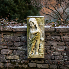 Statue of a angel on a stone wall with a natural background