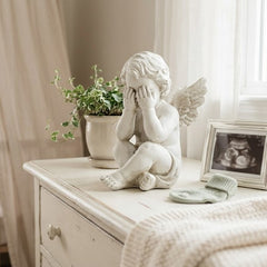 Nursery room with crib, statue, plant, and framed photo on a dresser.