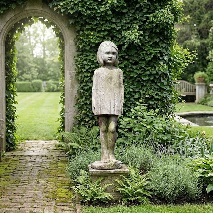 Statue of a child in a garden setting with an archway and pond in the background