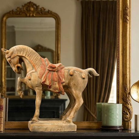 Decorative horse figure on a mantelpiece with books and candles in a room setting.