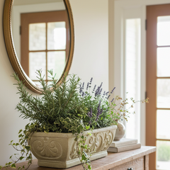 Decorative table with a large planter of greenery and flowers, a mirror above, and books on a white wall.